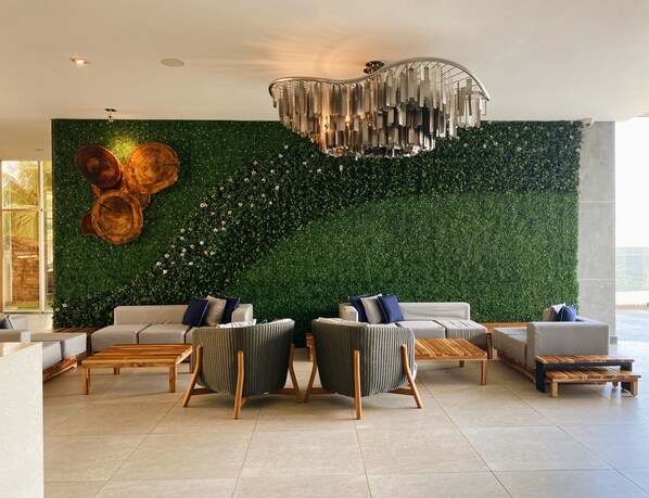 Una sala de estar moderna con una pared verde, dos sofás, sillas de mimbre y una mesa de centro de madera.