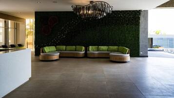 Un intérieur moderne avec un canapé d’angle, une table basse en verre et un mur décoratif orné d’un motif végétal vert.