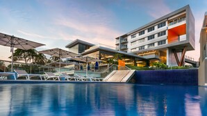 A modern hotel with a swimming pool, outdoor seating, and a multi-story building with balconies.
