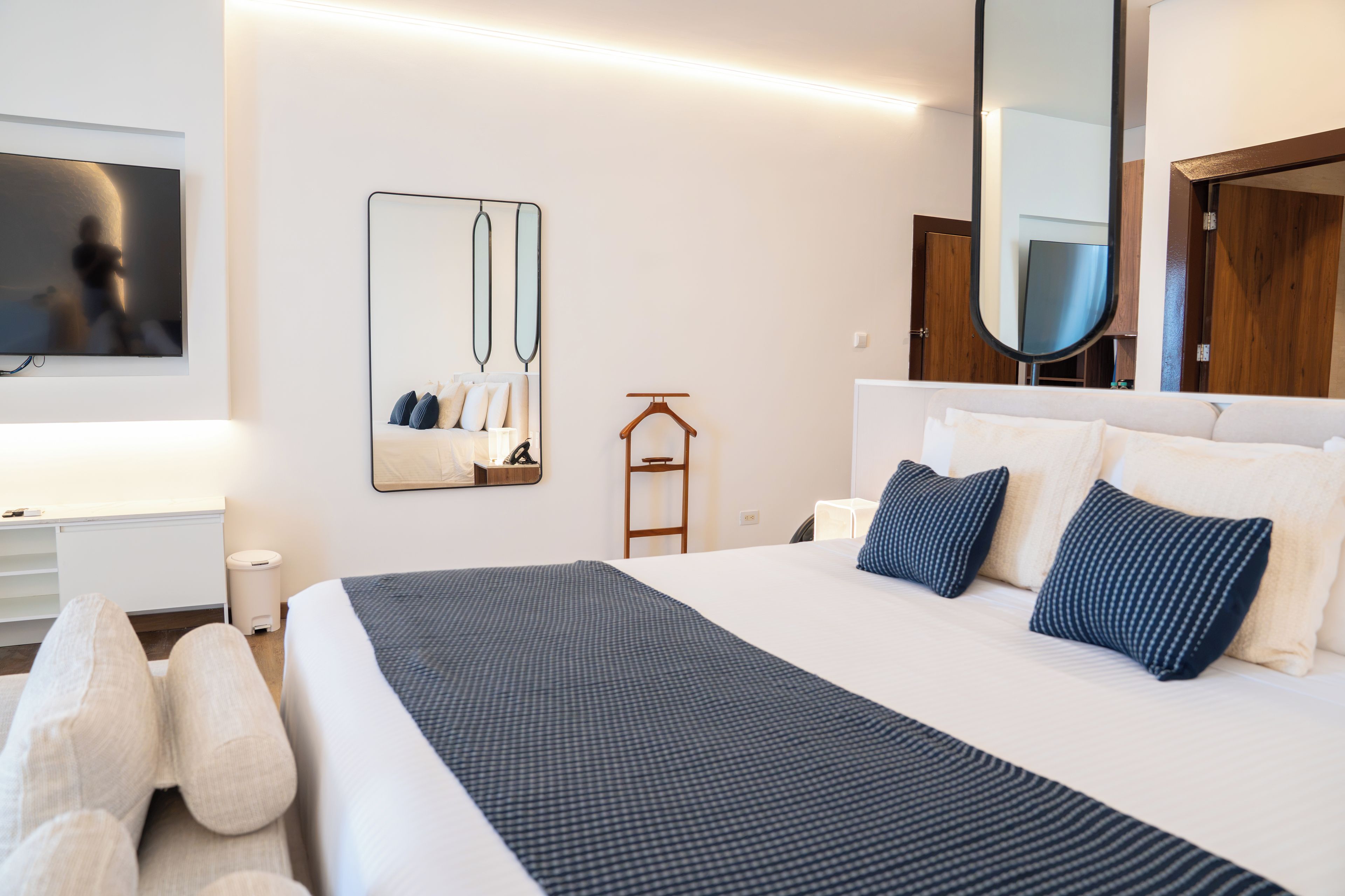 A modern hotel room with a large bed, bedside tables, a mirror, and a television.