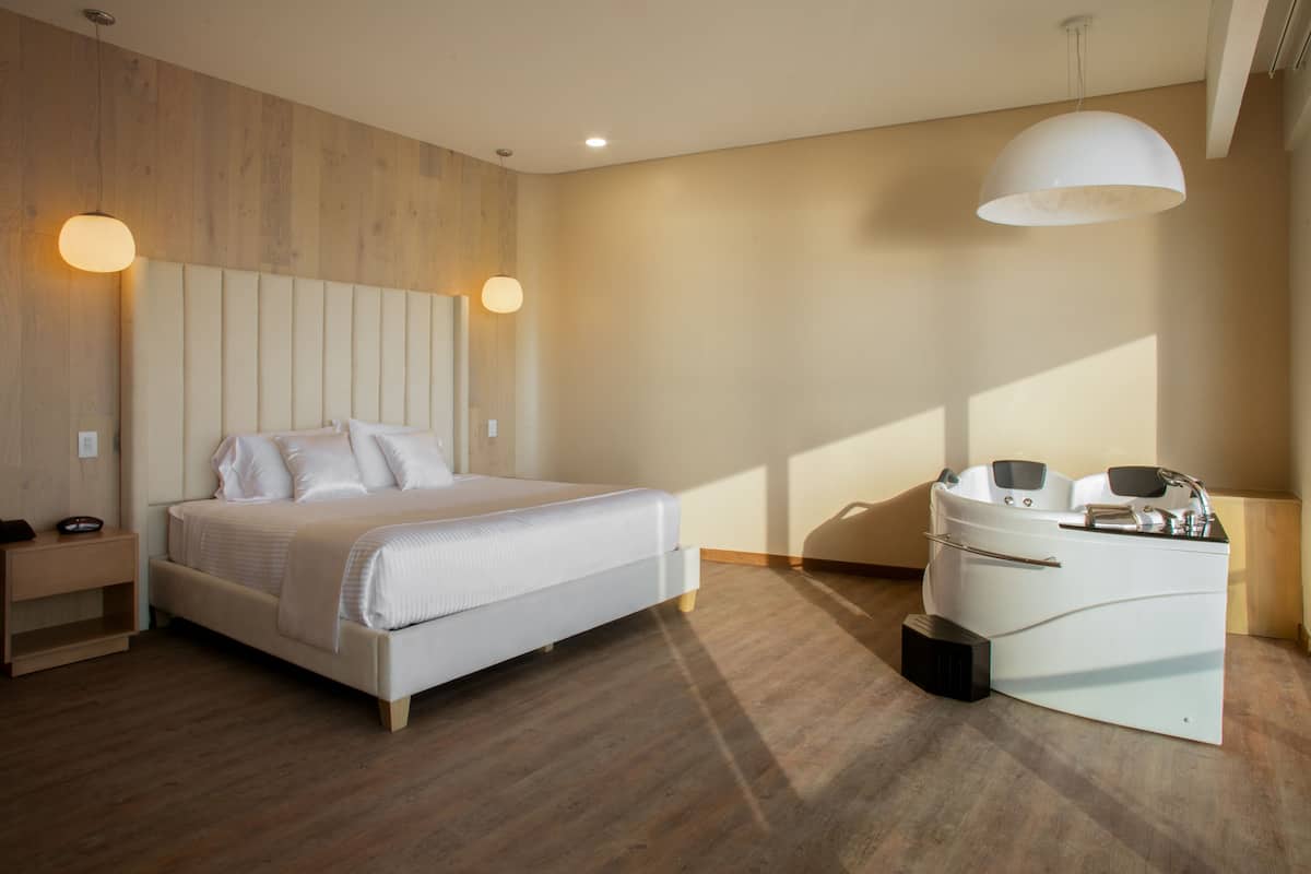 Une chambre moderne avec un grand lit, des tables de chevet, un banc intégré et une salle de bain séparée avec une baignoire.