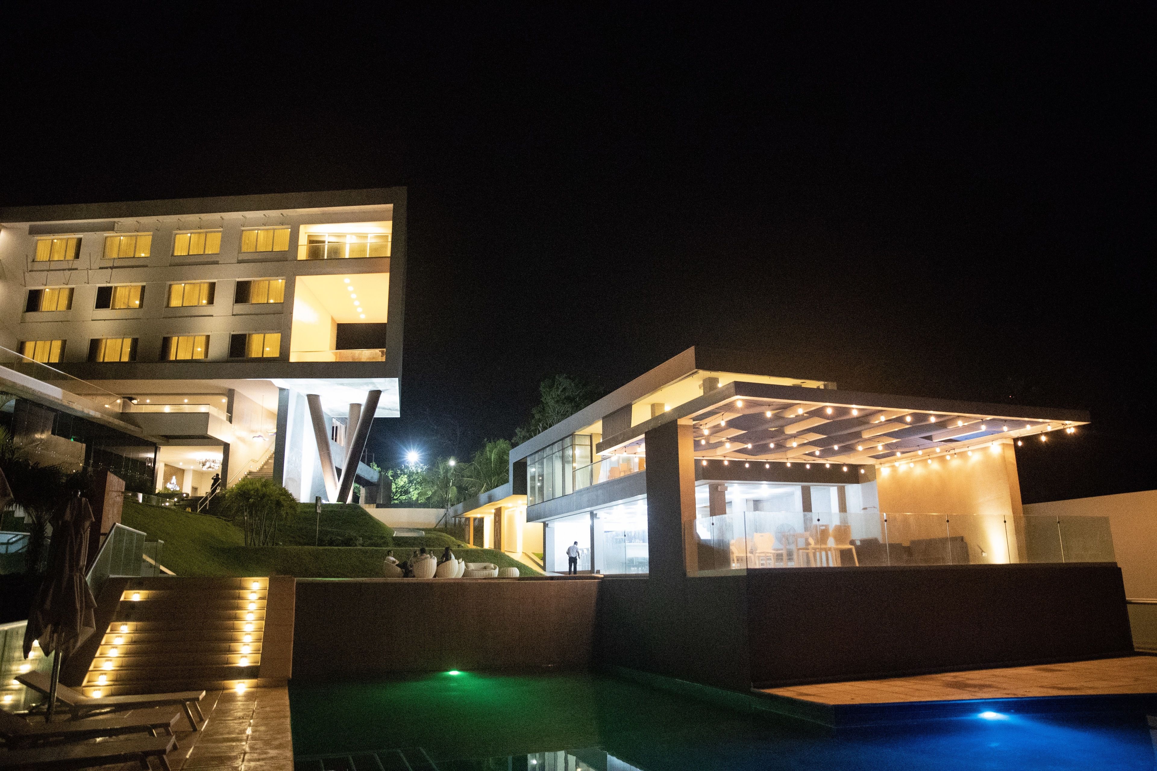 A modern hotel with a pool area, outdoor seating, and a well-lit entrance.