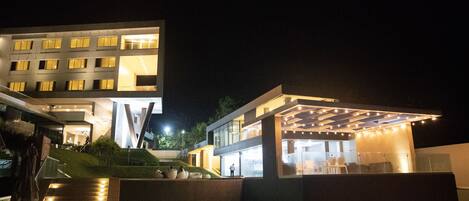A modern hotel with a pool area, outdoor seating, and a well-lit entrance.