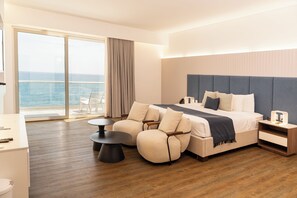 Een moderne hotelkamer met een groot bed, een balkon met uitzicht op zee, een zithoek met een tafel en stoelen, en een houten vloer.