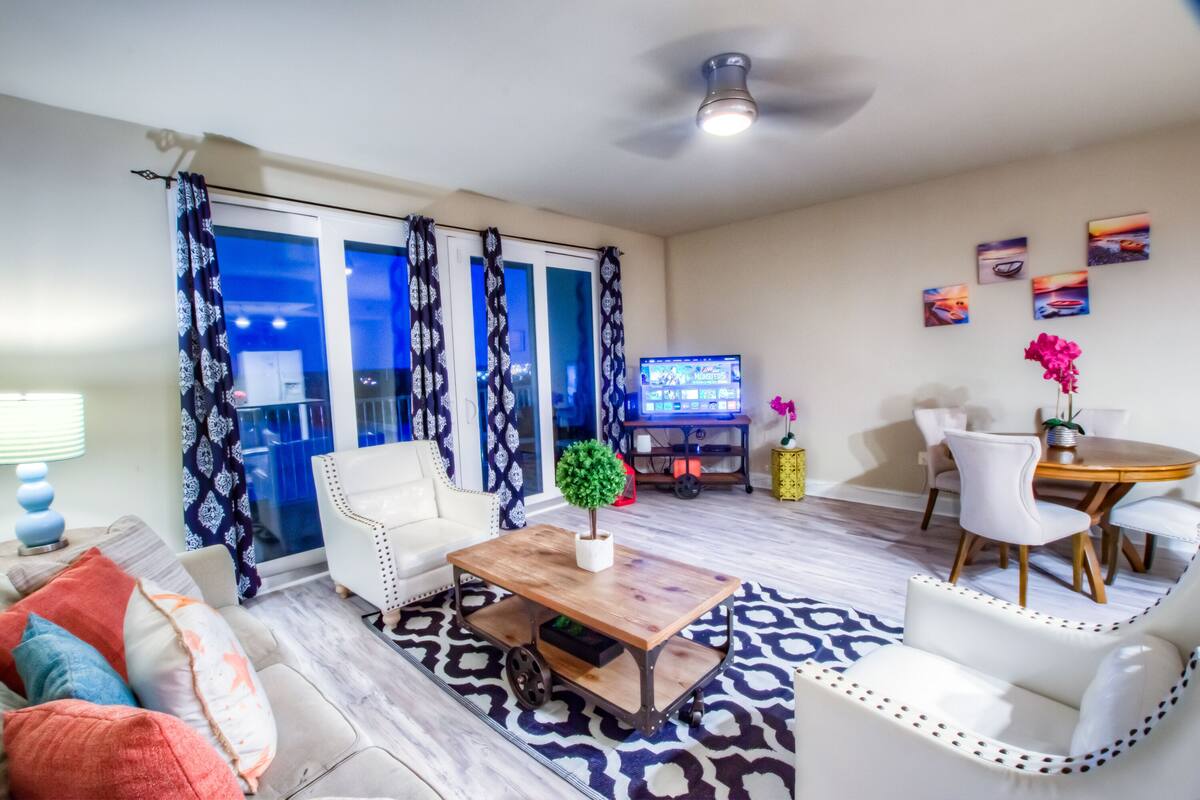 A living room with a sofa, coffee table, and a TV. There is a dining area with a table and chairs.