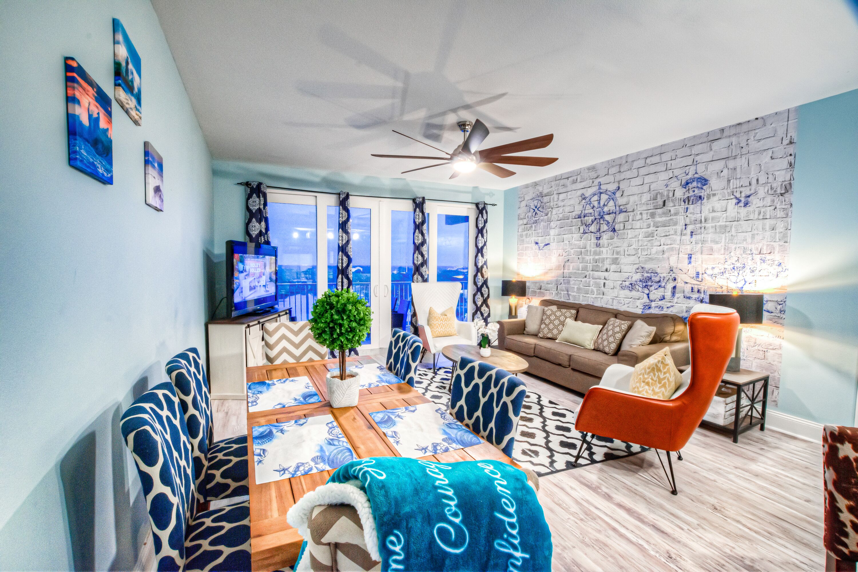 A living room with a sofa, armchair, and coffee table, a television, and a brick wall with nautical decor.