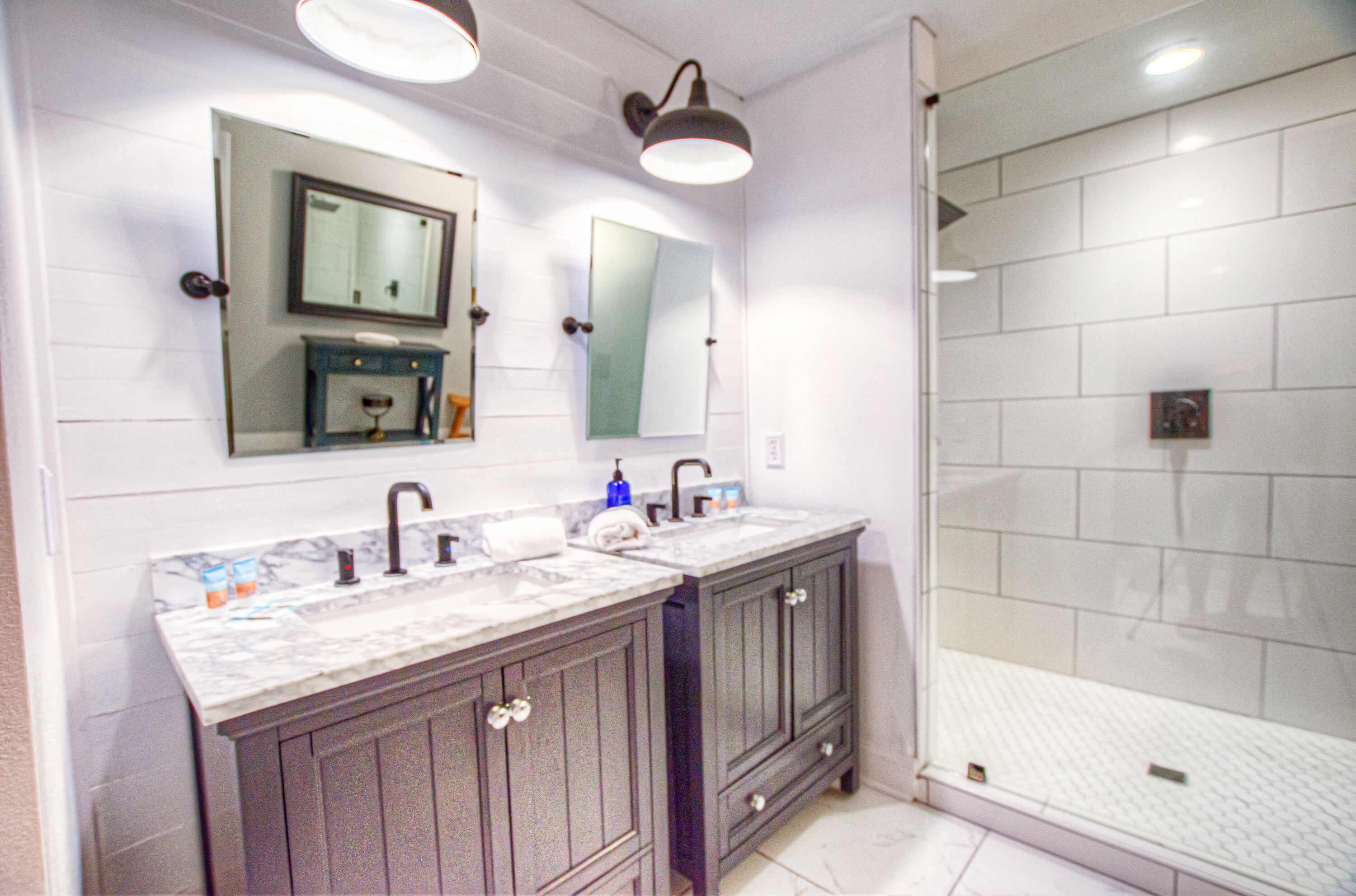 A bathroom with a double vanity, two mirrors, a shower, and a tiled floor.