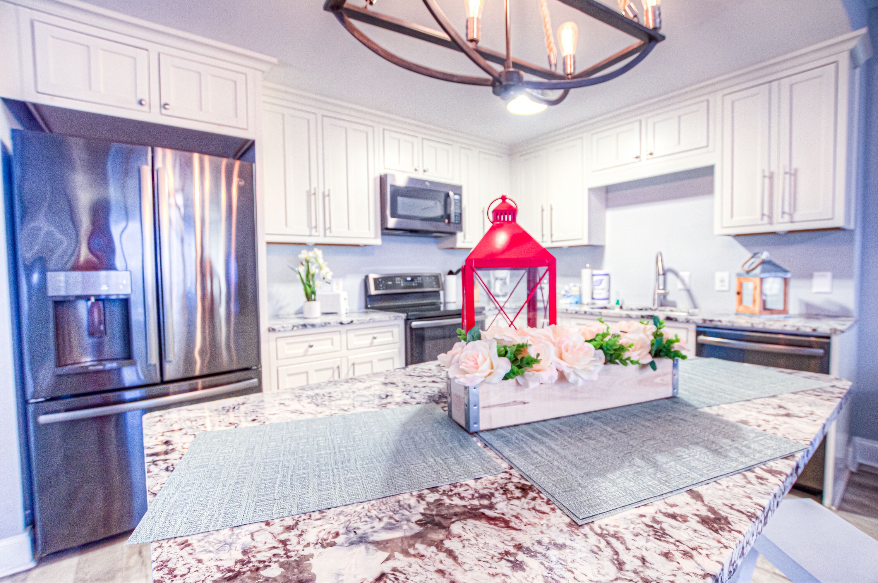 A modern kitchen with white cabinets, stainless steel appliances, and a marble countertop.