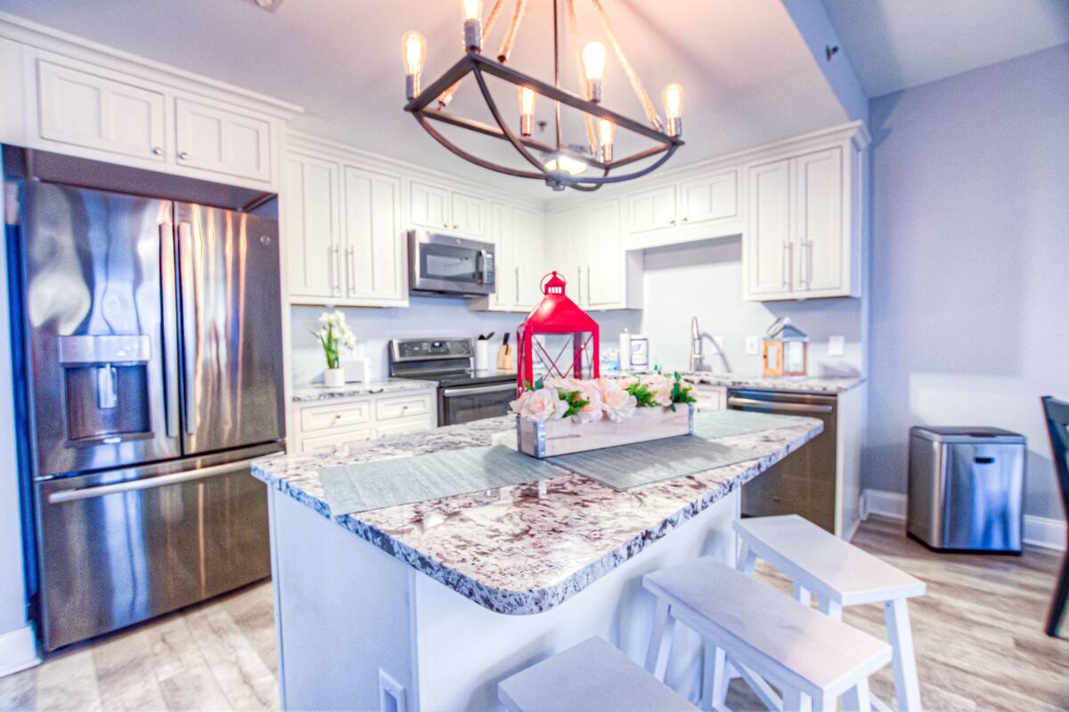 A modern kitchen with white cabinets, stainless steel appliances, a marble island, and a red pendant light.