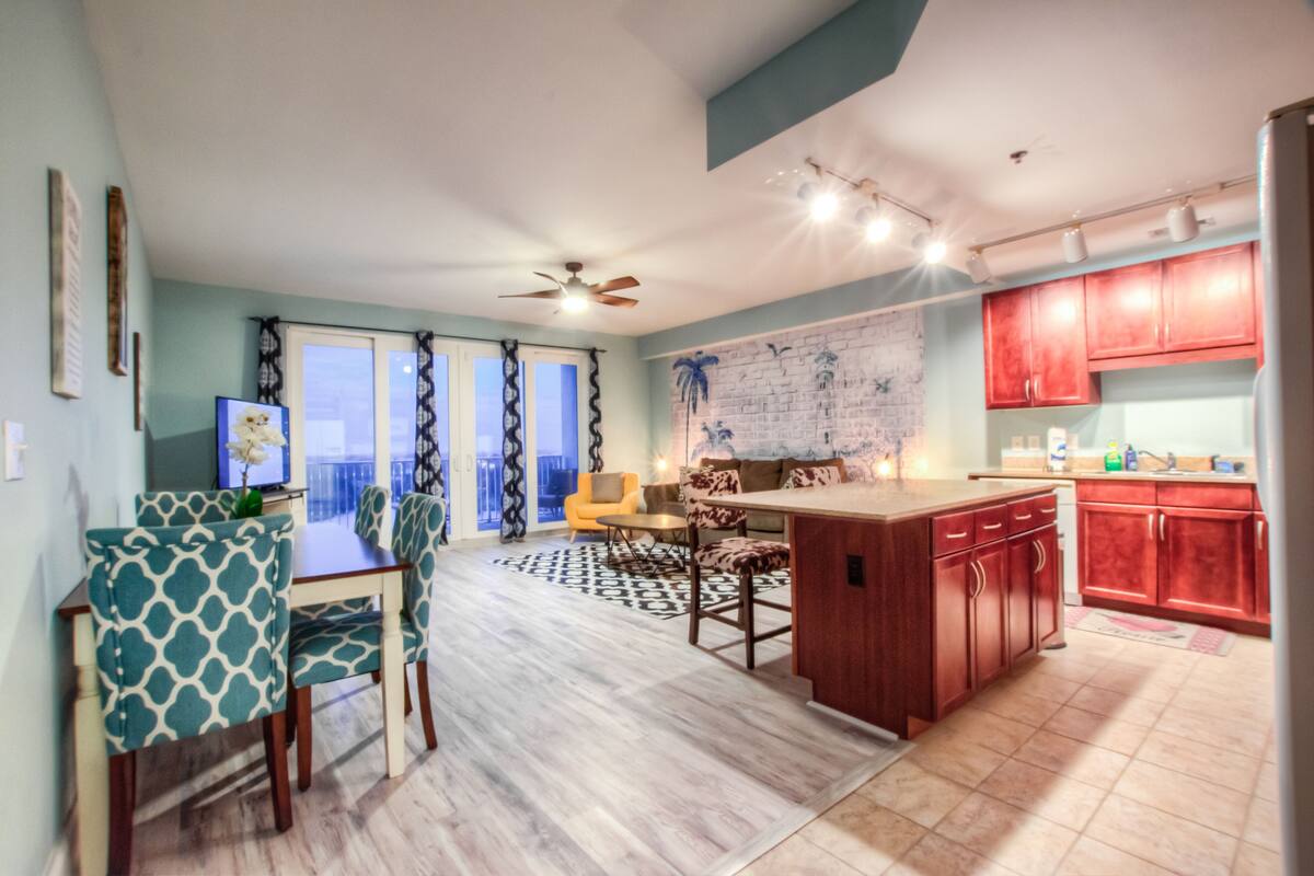 A modern kitchen with red cabinets, a dining area with patterned chairs, and a large window with curtains.