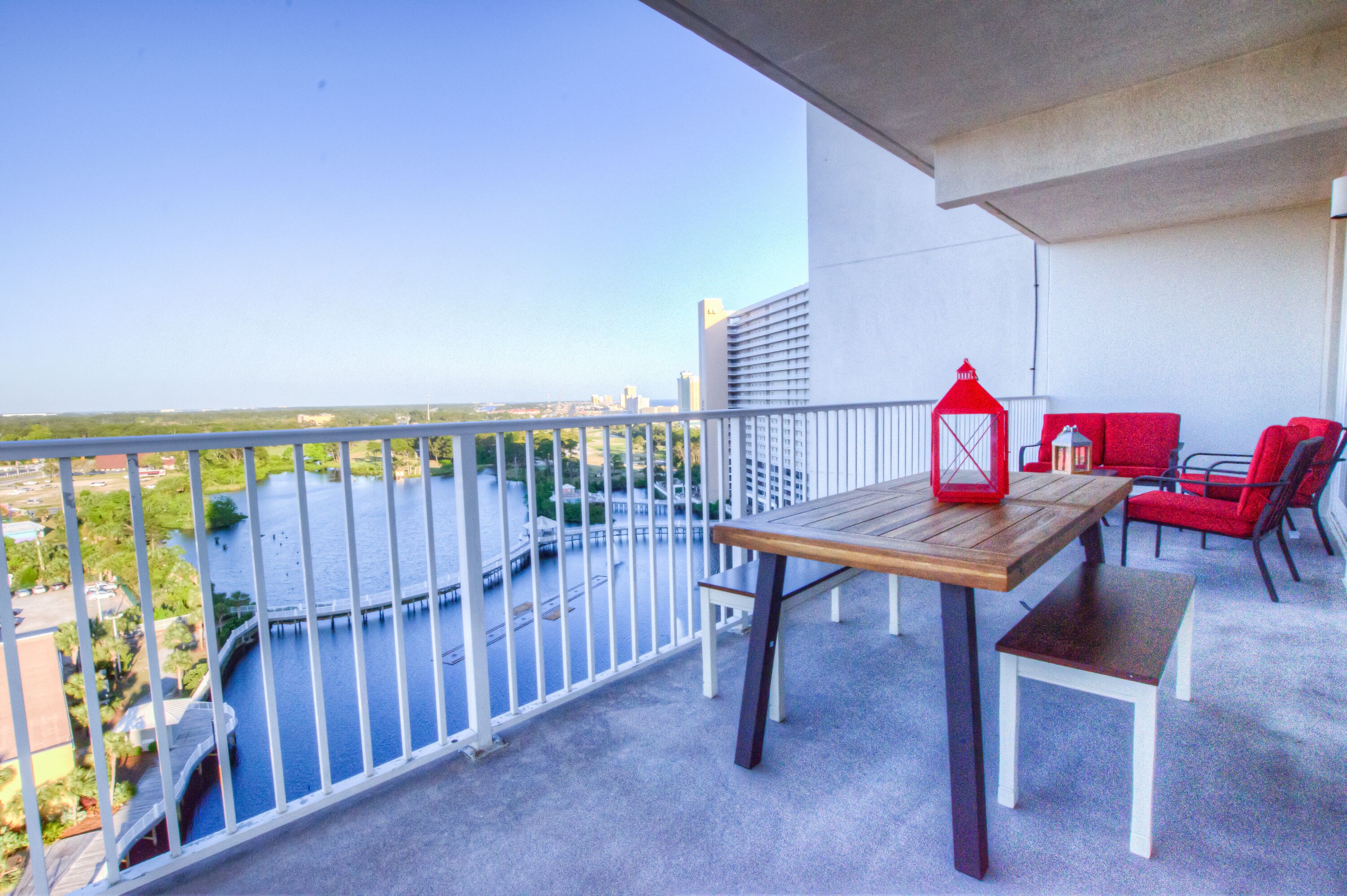 A balcony with a view of a river, a wooden table, red chairs, and a red lantern.