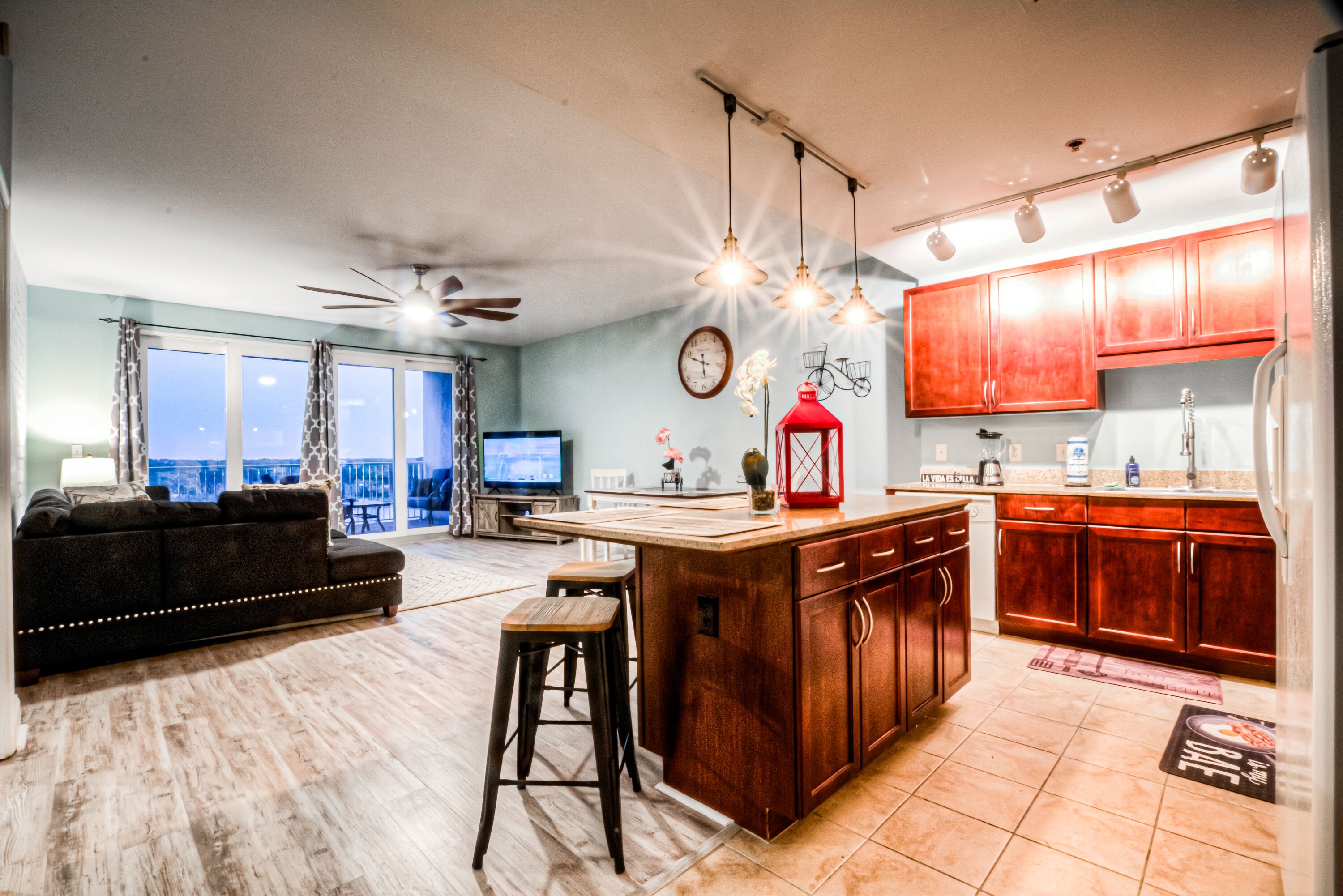 A modern kitchen with wooden cabinets, a central island, and a dining area with a sofa and bar stools.