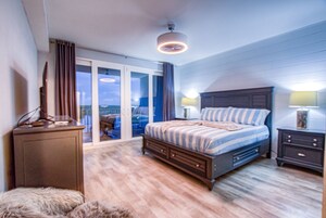Ein Schlafzimmer mit einem großen Bett, einem Schminktisch, einem Nachttisch und Blick durch eine Schiebetür ins Freie.
