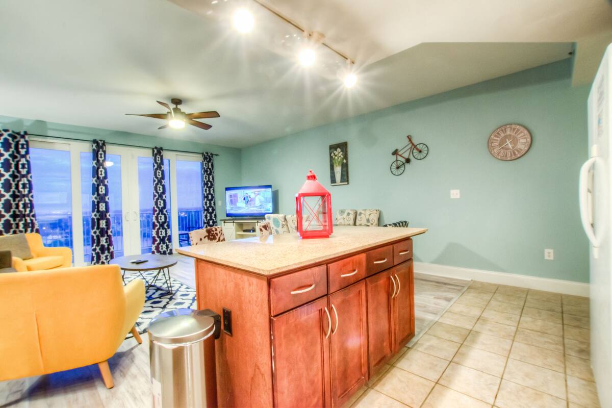 A modern kitchen with a wooden island, a dining area with a yellow chair, a television, and a bicycle on the wall.