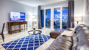 Una sala de estar moderna con un sofá de cuero, un televisor, una mesa redonda para café y vistas de la ciudad a través de amplios ventanales.
