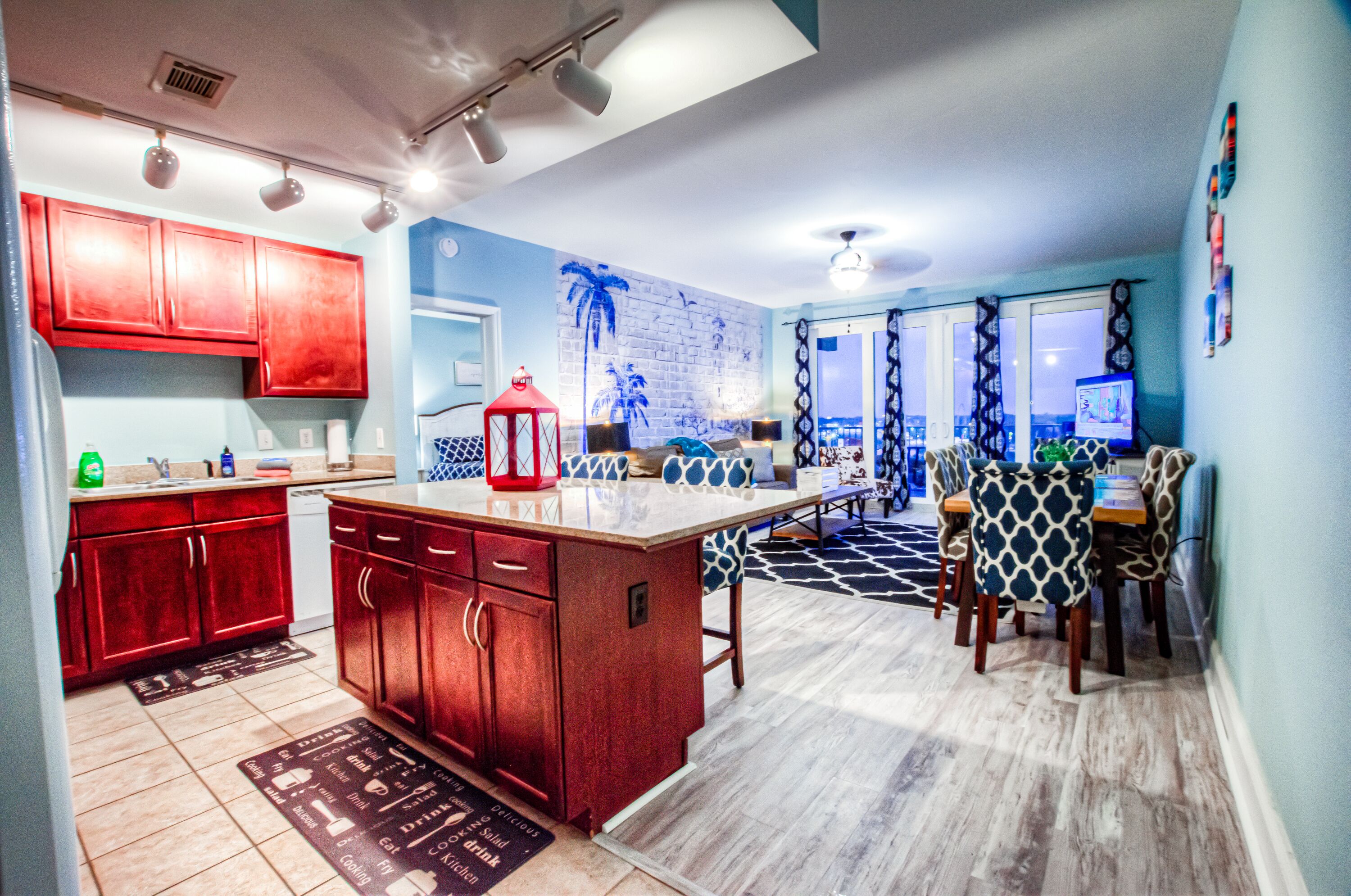 A modern kitchen with red cabinets, a central island, and a dining area with patterned chairs.