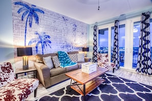 A living room with a brick wall mural, a sofa, a coffee table, and a view through large glass doors.