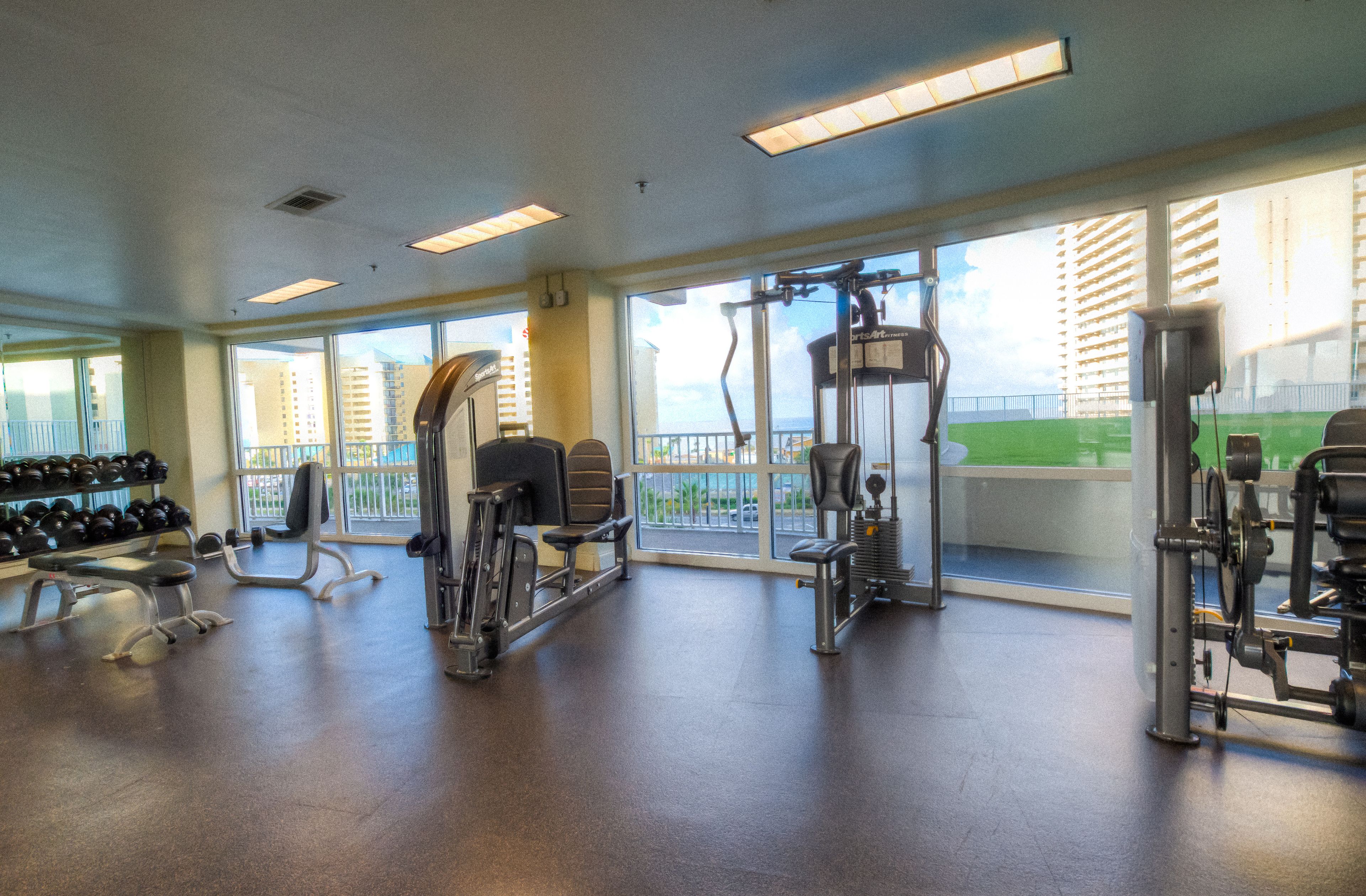 A gym with various exercise equipment, large windows, and a view of a building outside.