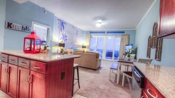 Una cocina con una isla roja, una zona de comedor con una mesa y sillas, un sofá, y vistas al exterior a través de una puerta corredera.