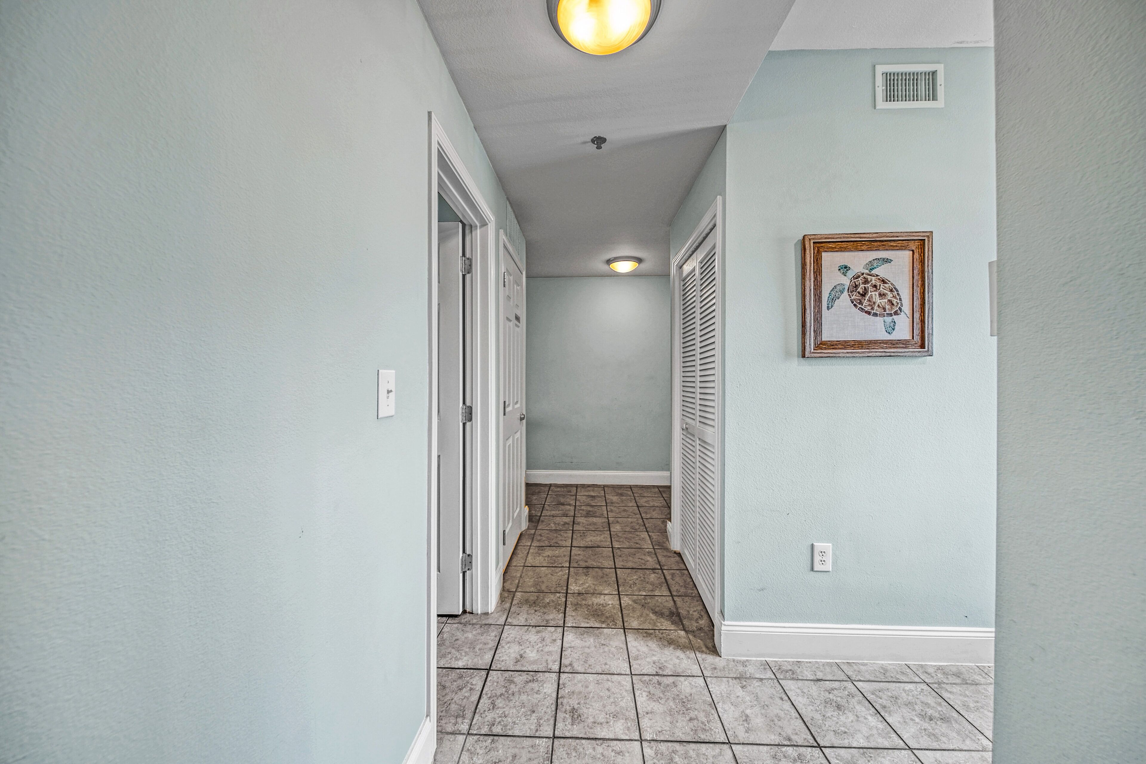 A hallway with light blue walls, a tiled floor, and a framed turtle picture on the wall.