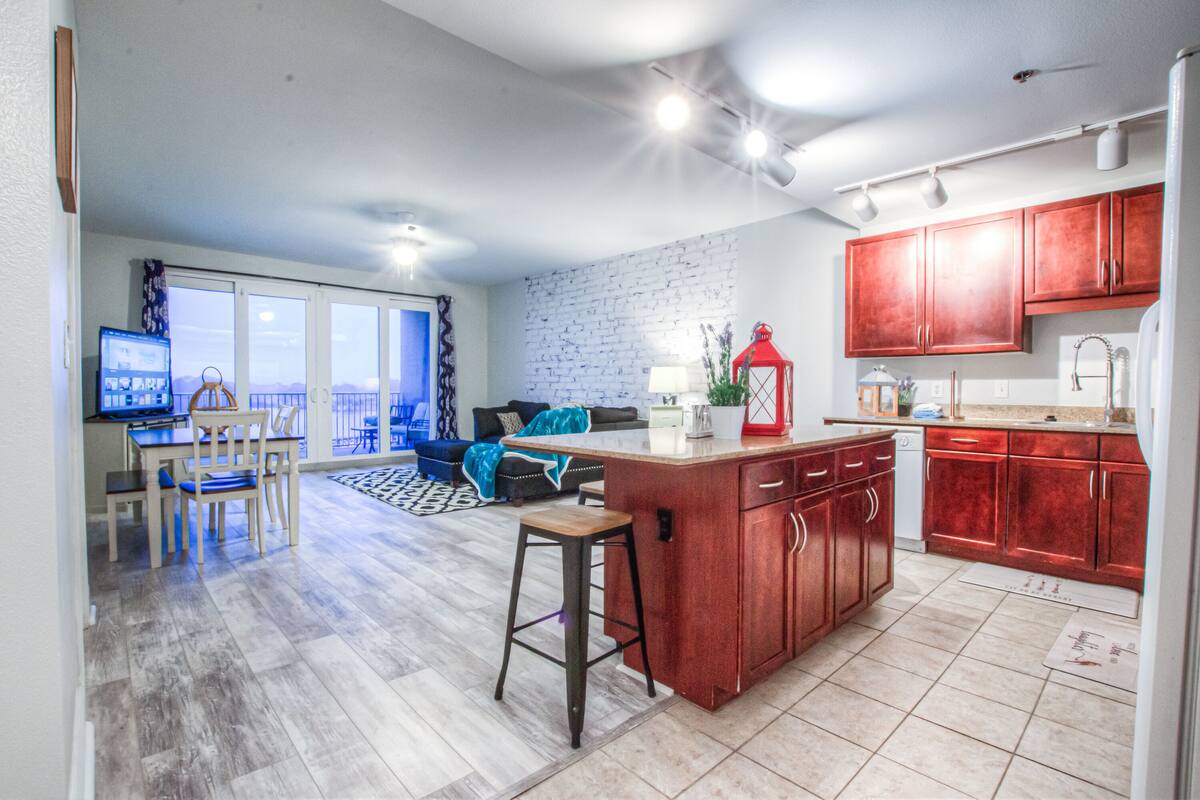 A modern kitchen with wooden cabinets, a central island, and a dining area with a blue sofa and chairs.
