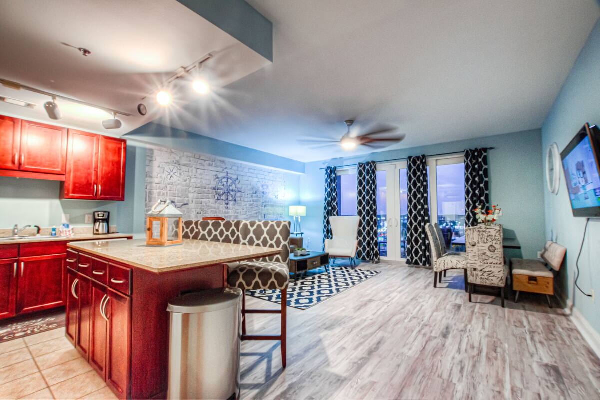 A modern kitchen with red cabinets, a central island, and a dining area with patterned chairs.