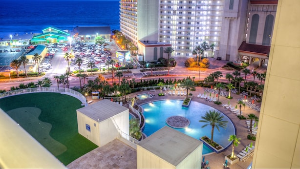 Un hotel con piscina, vista al océano y un estacionamiento con coches.