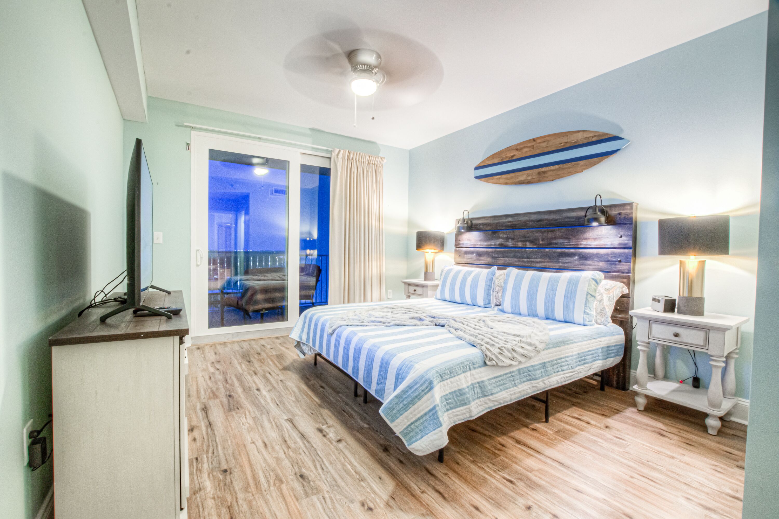 Un dormitorio con cama, escritorio, silla, ventilador de techo y vistas al exterior.