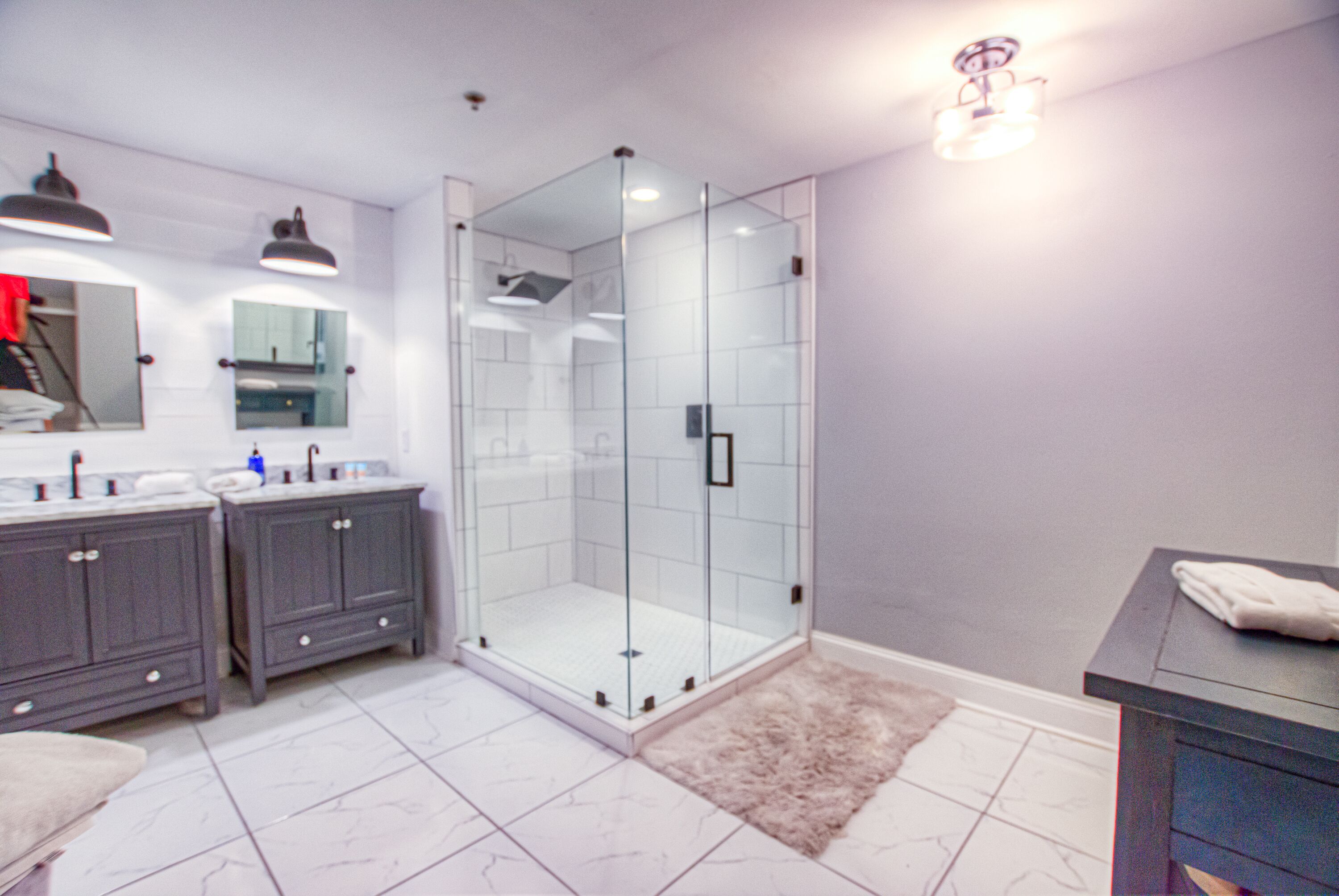 Une salle de bain moderne avec une douche à parois de verre, deux vasques avec miroirs et un tapis moelleux sur le sol.