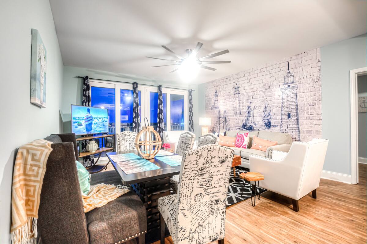 A modern living room with a dining area, a ceiling fan, and a brick-patterned wall.