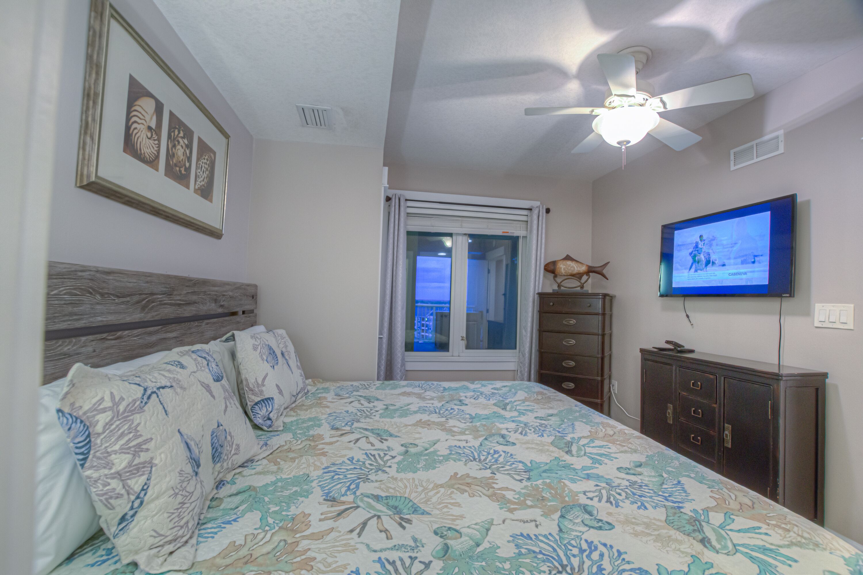 Un dormitorio con cama, ventilador de techo, televisión y ventana.