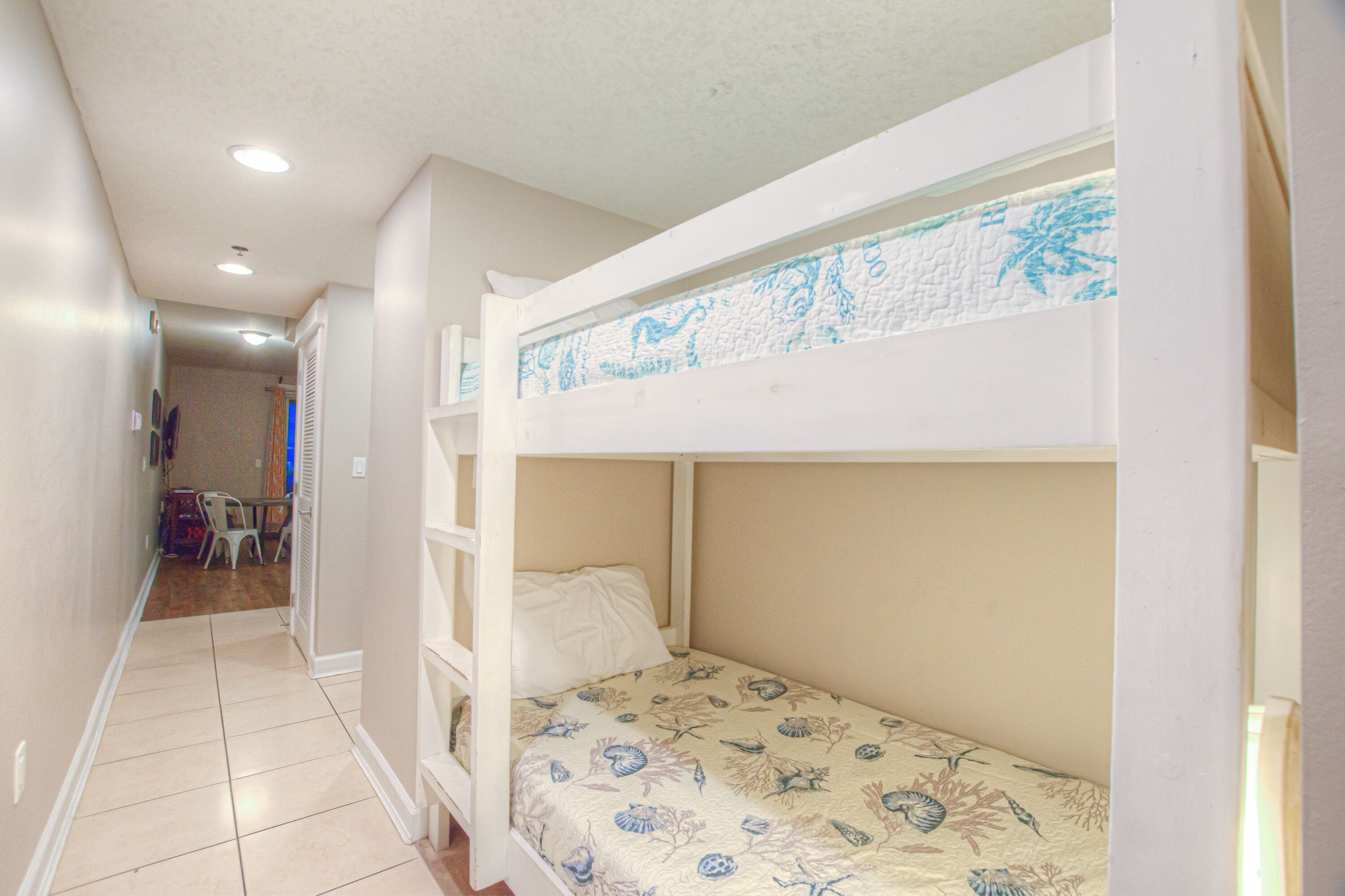 A bunk bed with floral bedding in a hallway with a tiled floor and a door leading to another room.