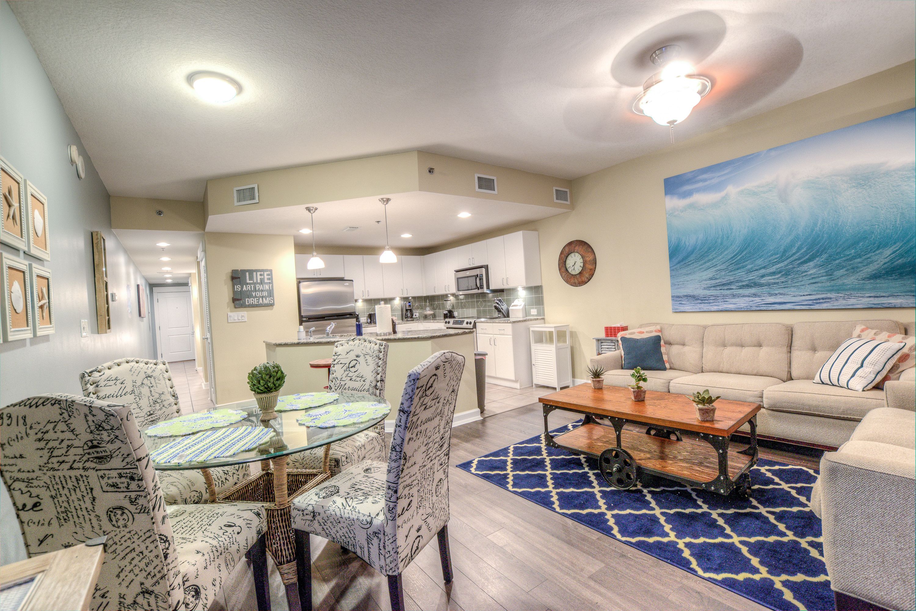 A spacious living area with a dining table, chairs, a sofa, and a kitchen in the background.
