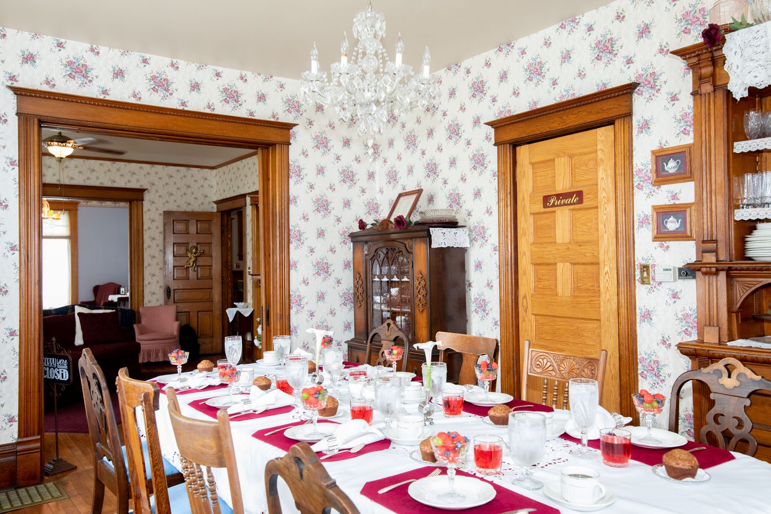 A dining room with a table set for a meal, surrounded by floral wallpaper and wooden furniture.