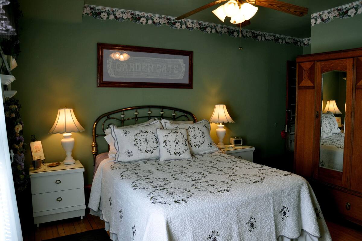 Ein Schlafzimmer mit einem Bett, zwei Nachttischen, einem Schrank und einem gerahmten Bild an der Wand.