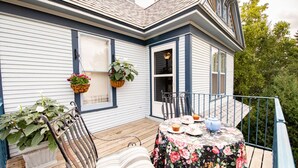 A wooden deck with a table set for tea, surrounded by potted plants and a chair. - Garden Gate BnB (Sturgeon Bay)