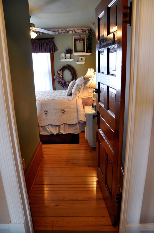 A narrow hallway leading to a bedroom with a bed, dresser, and a small window. - Garden Gate BnB (Sturgeon Bay)