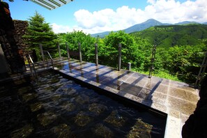 Una piscina con borde de piedra y postes de madera, rodeada de exuberante vegetación y una montaña al fondo.