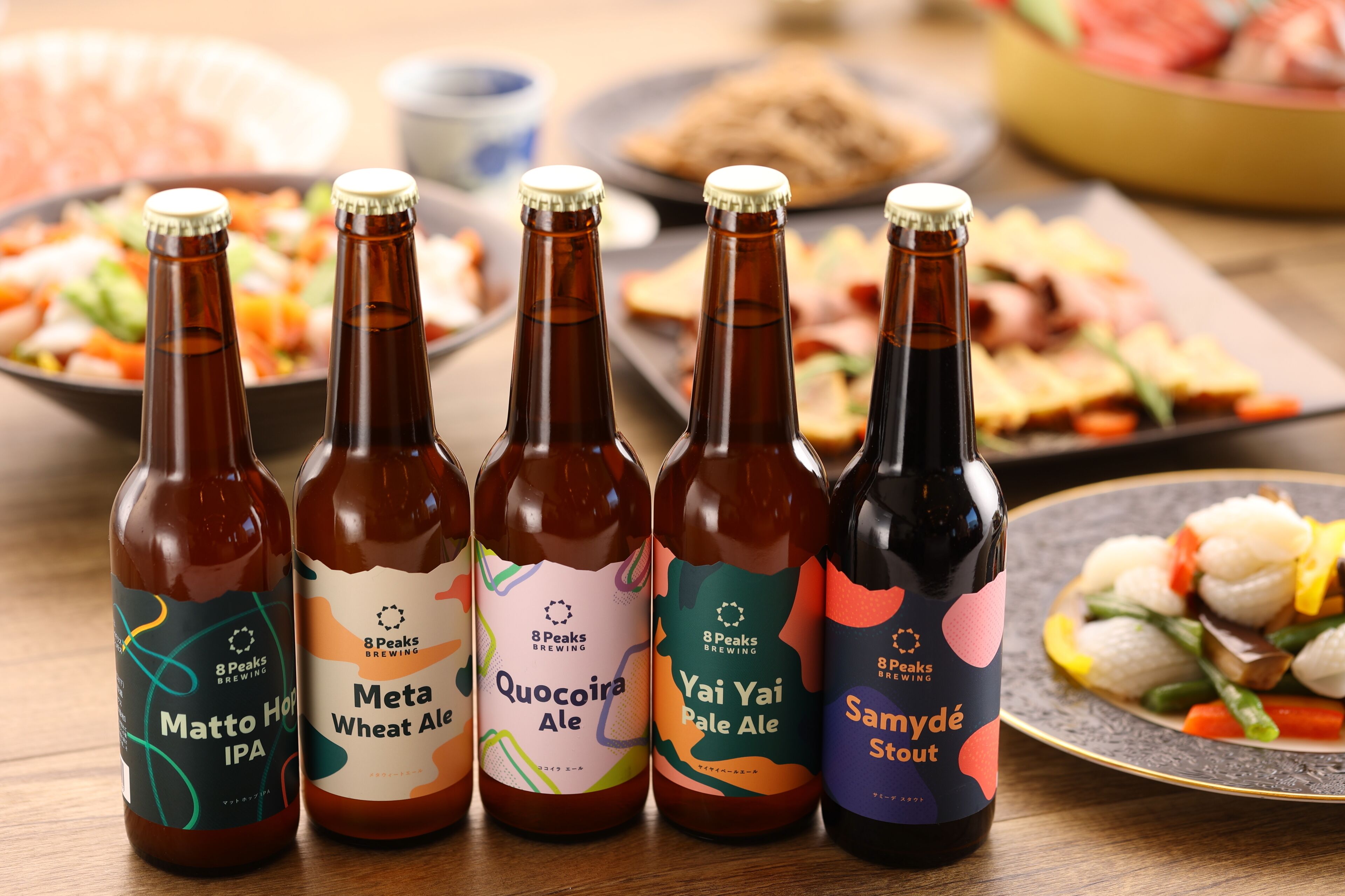 Four bottles of beer with labels, placed on a table with various dishes in the background.