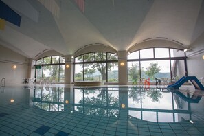 An indoor swimming pool with clear views of trees and hills through large windows.