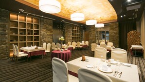 Een restaurant met meerdere tafels, elk gedekt met witte tafelkleden en stoelen, en een plafond met een bloemenmotief.