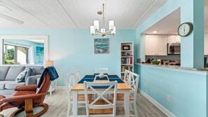 Un salon moderne avec un canapé gris, un fauteuil à bascule en bois et une table à manger avec des chaises blanches.