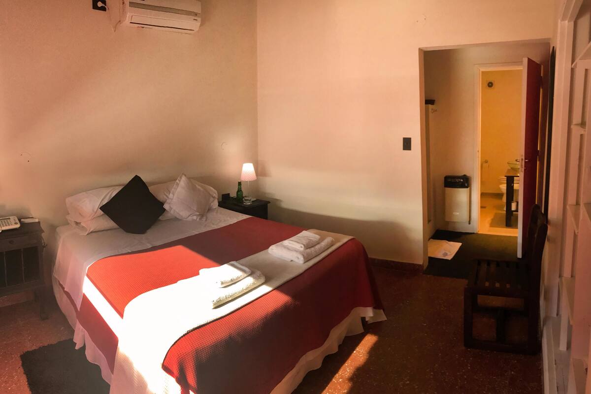 Quarto de hotel com cama, mesa de cabeceira, abajur e uma cadeira.