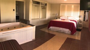 A hotel room with a large bed, a separate bathroom with a bathtub, a walk-in closet, and a television. - Casa Alta Hotel Boutique Solo Adultos (Villa Carlos Paz)