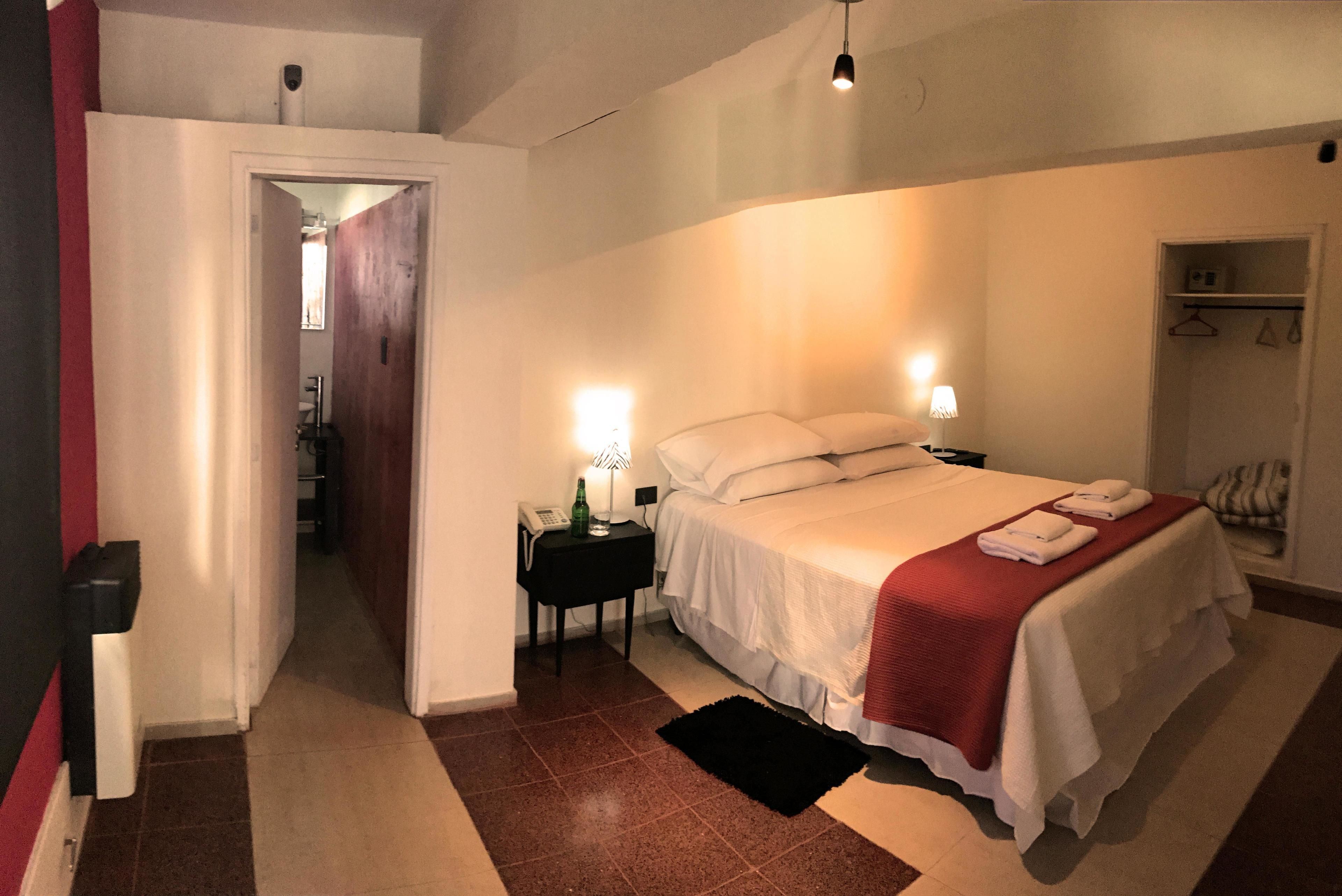Ein Hotelzimmer mit Bett, Nachttischlampen, einem Nachttisch, einer roten Tagesdecke und einem Kleiderhaken.