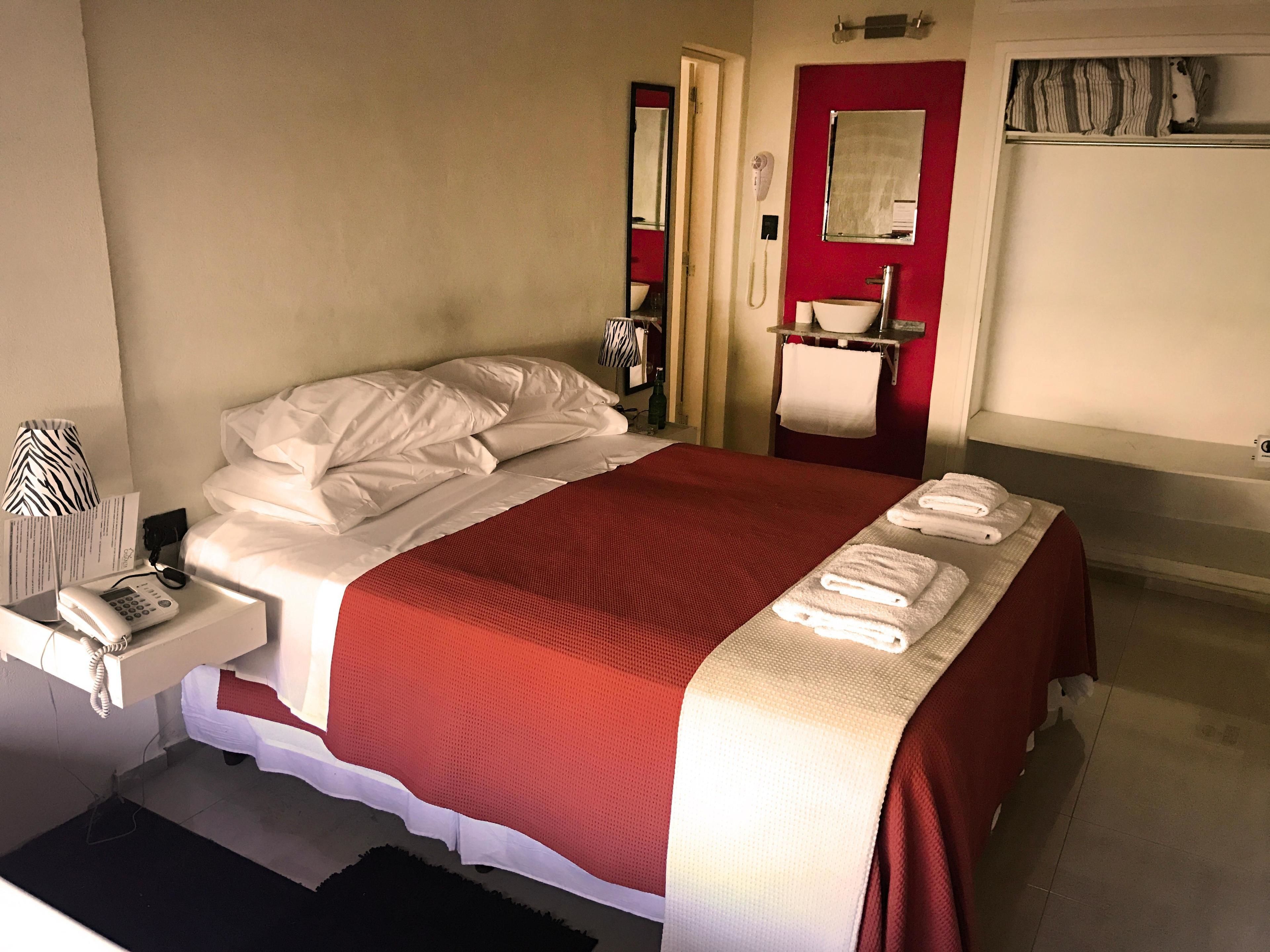 Une chambre d’hôtel avec un lit, un téléphone sur la table de chevet, une couverture rouge et un porte-serviettes avec des serviettes.