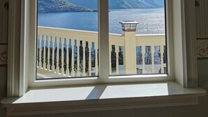 Une fenêtre donnant sur une montagne et un lac, un drapeau et une rambarde de balcon.