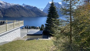 Une vue sur le lac, avec une terrasse en bois, des marches en pierre et un panorama sur des montagnes enneigées.