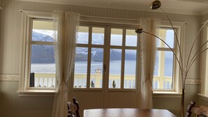 Un coin repas avec une grande table en bois, deux chaises et une vue sur un lac, avec des montagnes en arrière-plan.