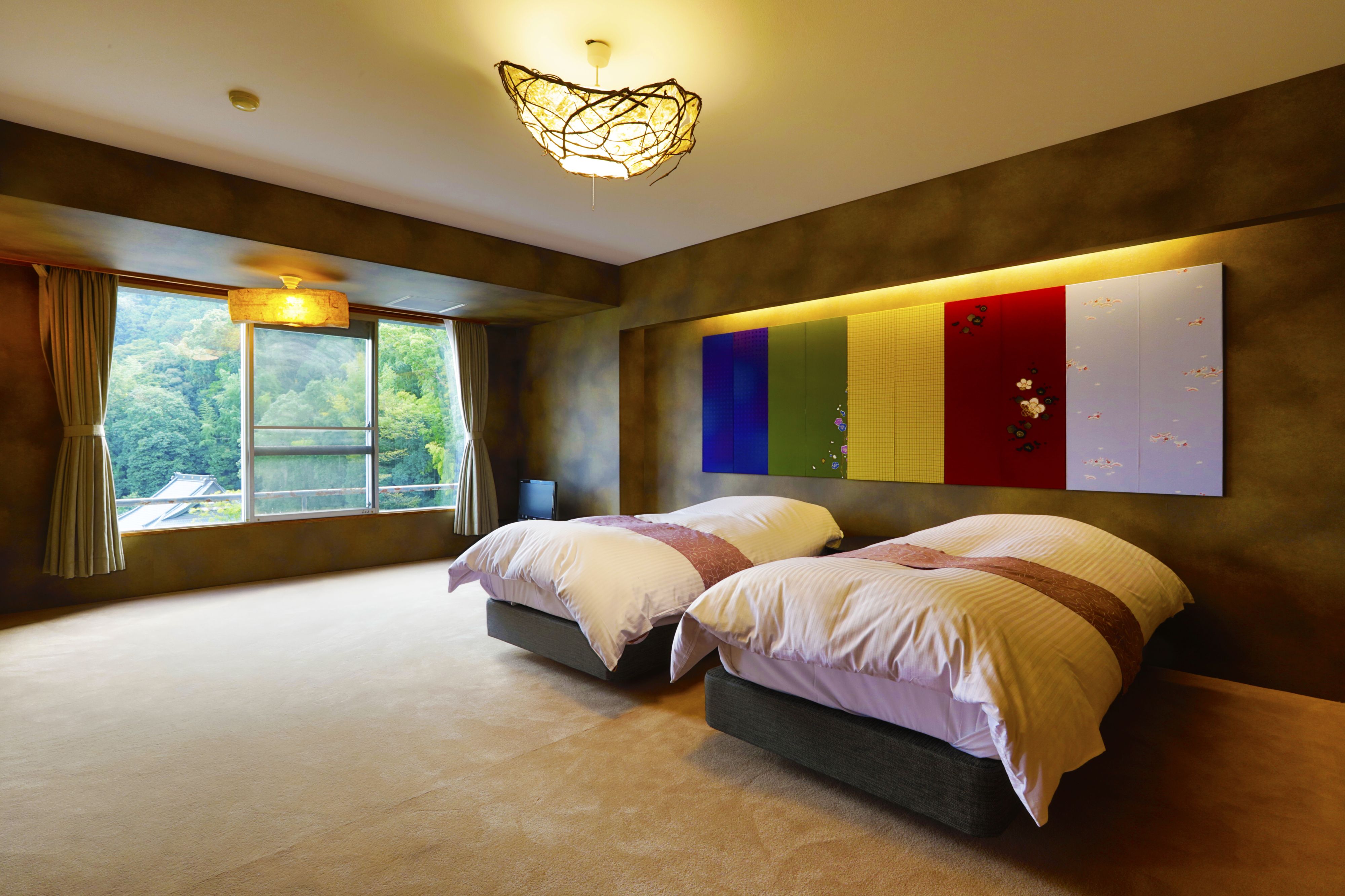 A bedroom with two beds, a large window, and a wall-mounted light fixture.